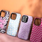 phone cases "Four stylish phone cases displayed on a split orange and pink background. From left to right: a black and white zebra print case with a pink 3D 'LOVE' text, a blue checkered case with white daisy flowers, a lavender case with small white daisies (with phone inside), and a pink case with wavy magenta stripes. All cases feature the 'coverismo' branding.