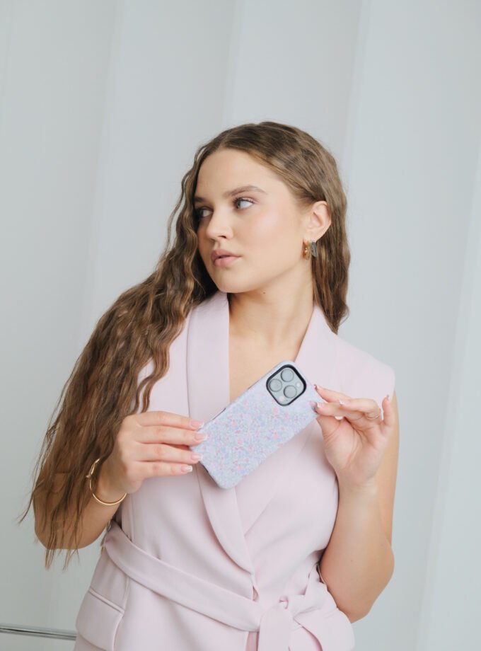 A phone case with a soft floral pattern featuring pink, purple, and blue flowers, placed on a white surface surrounded by pastel-colored sticky notes, colored pencils, and a purple-lined notebook.